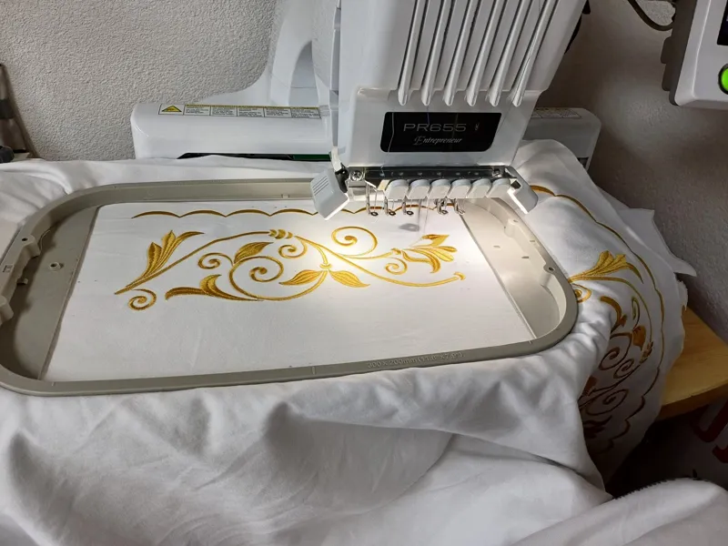 Vyšívací stroj vyšíva zlatý ornament na biely textil